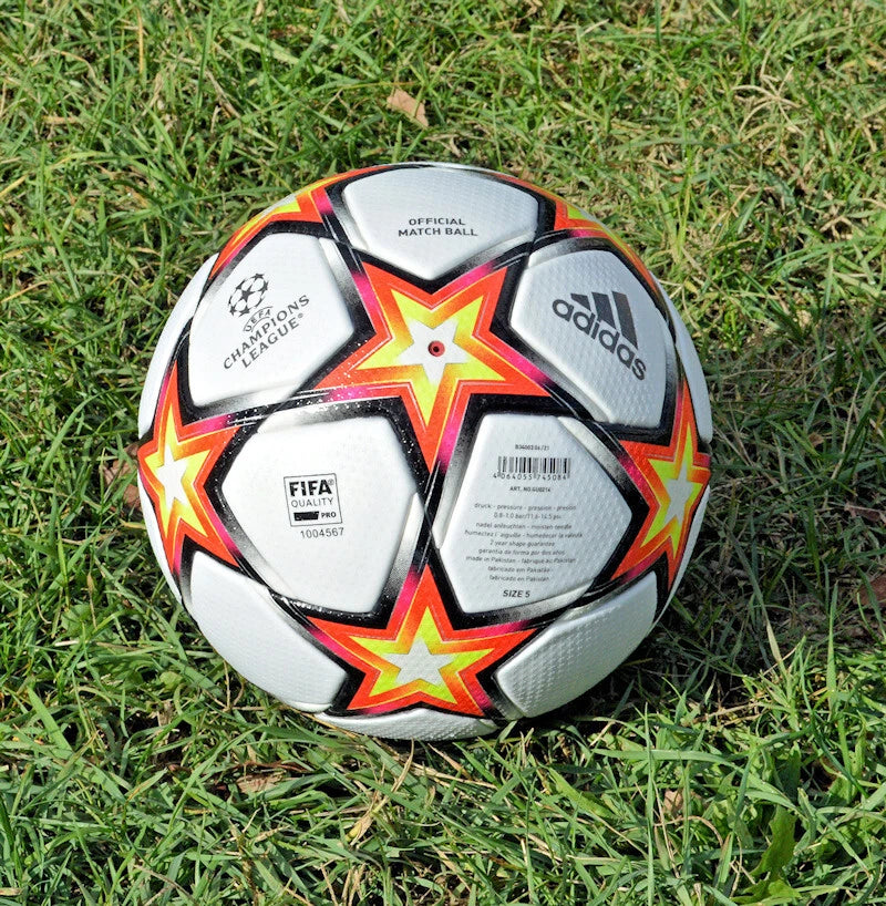 Pallone Adidas UCL 2021-2022 – dettaglio punte stella rosse e giallo fluo su erba